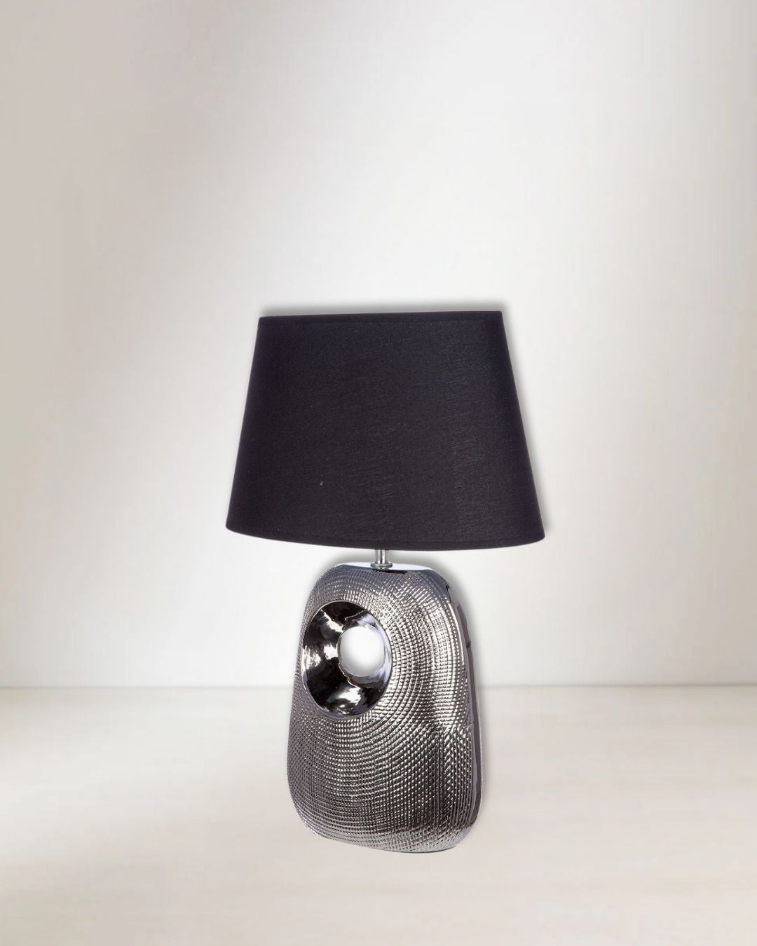 Tischlampe „Manisa“ mit silbernem Keramikfuß und ovalem, konischen Lampenschirm.